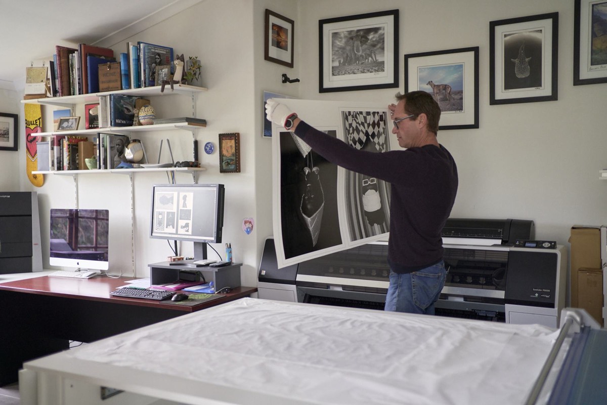 The VvG studio: Vincent holding up a large black and white print in front of the Epson P9000, framed photographs and bookshelves on the walls