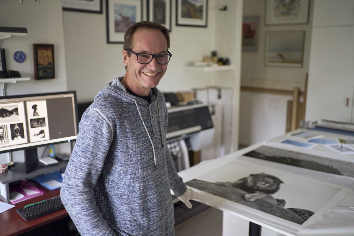 Vincent van Graan smiling in his studio, one gloved hand on a large print lying on the table