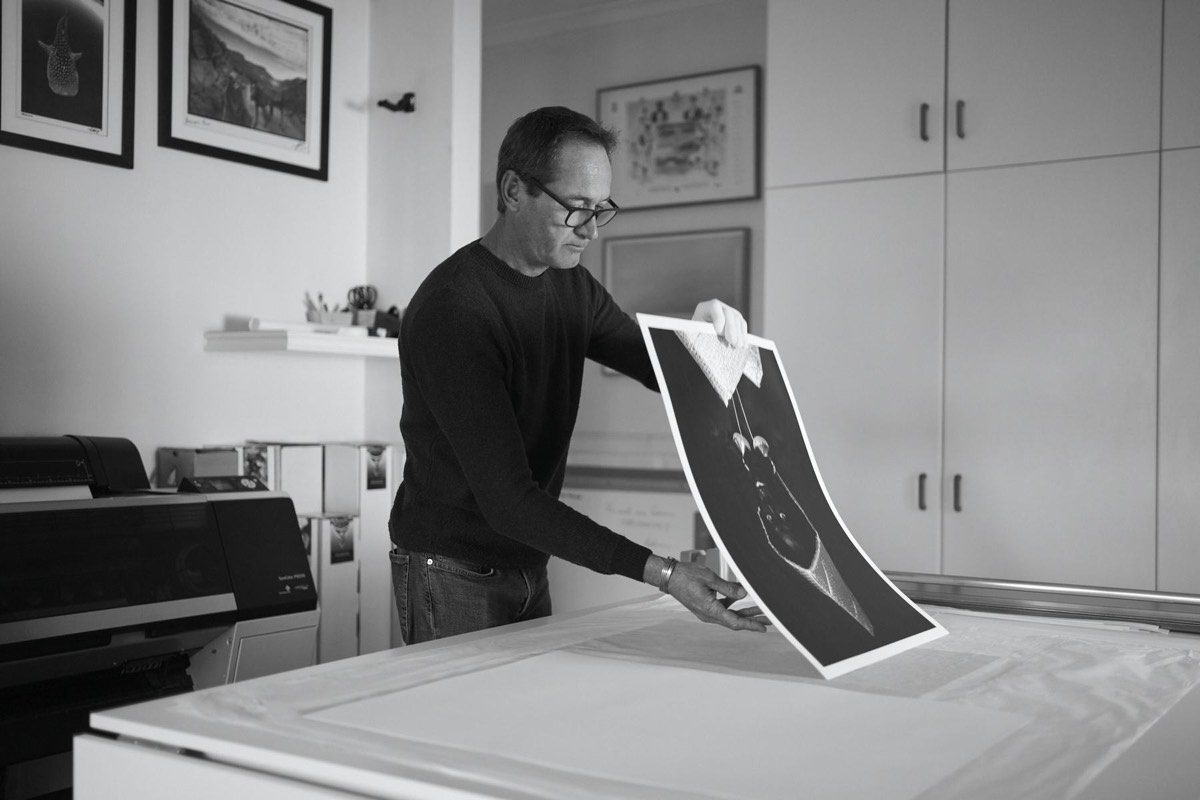 Vincent holding a freshly printed black and white photograph up to the light in the studio, printer and cabinets behind him